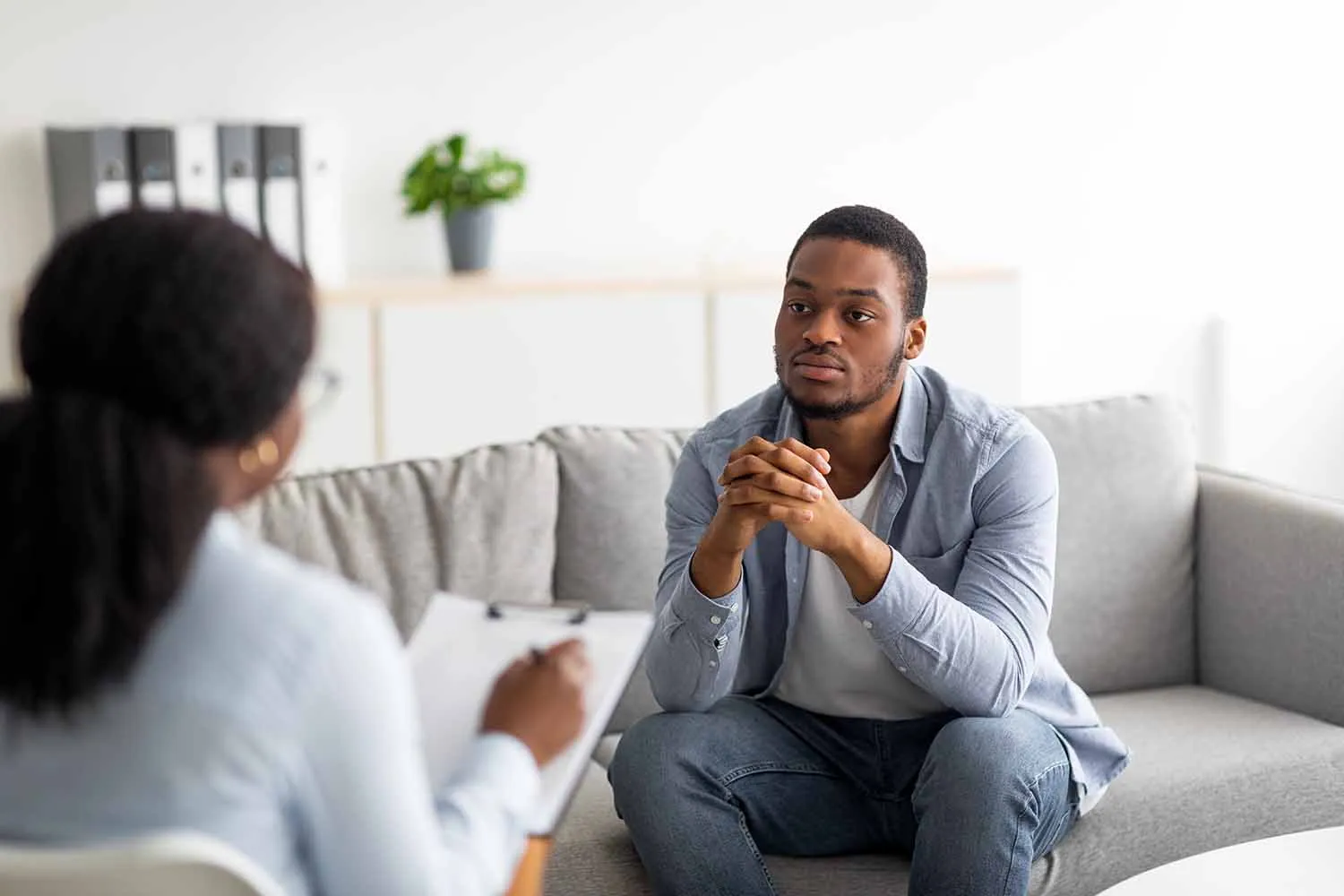 A counselor taking notes while talking with a client on a couch.